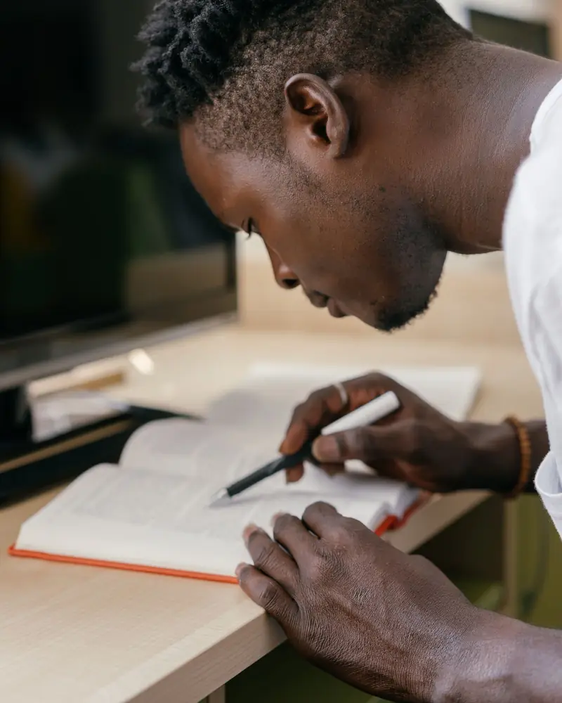 Un jeune homme concentré écrit dans son cahier.