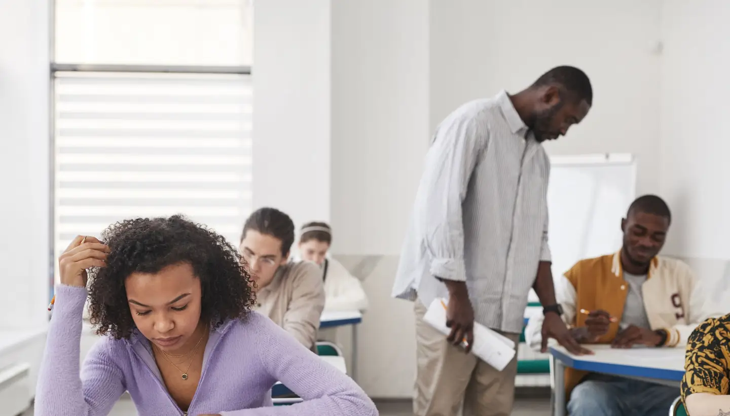 Des étudiants composent dans une salle d'examen à l'université, un surveillant passe entre les tables.